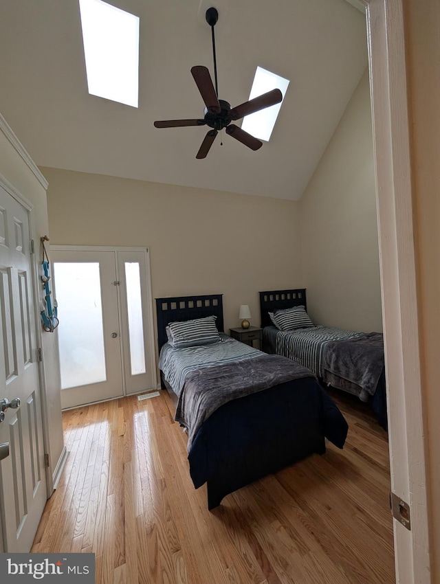 bedroom featuring ceiling fan, vaulted ceiling with skylight, light wood-type flooring, and access to exterior