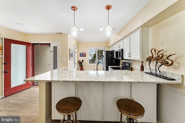 kitchen with light stone counters, stainless steel microwave, electric range, freestanding refrigerator, and a peninsula