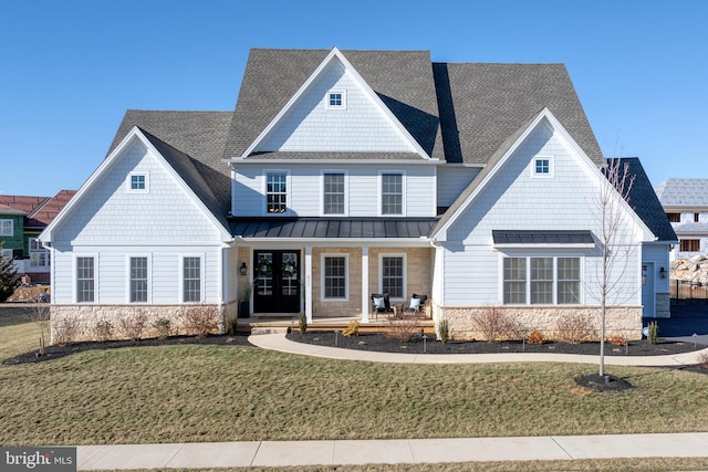 view of front of home with a standing seam roof, stone siding, covered porch, roof with shingles, and a front yard