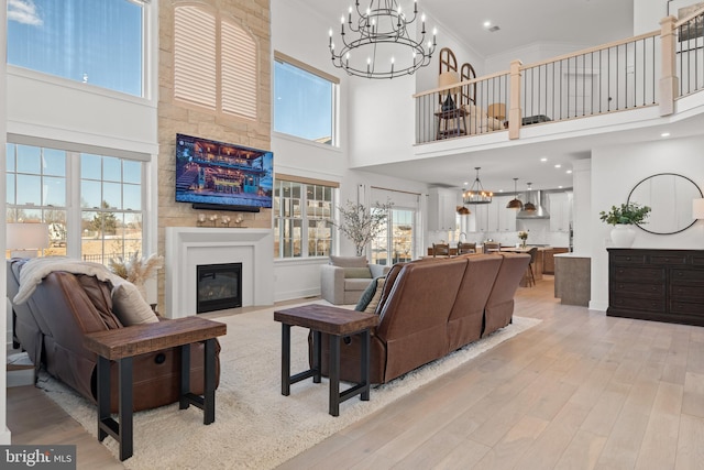 living area with a glass covered fireplace, a wealth of natural light, a chandelier, and light wood finished floors