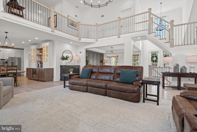 living room with an inviting chandelier, light wood-style floors, baseboards, and ornamental molding