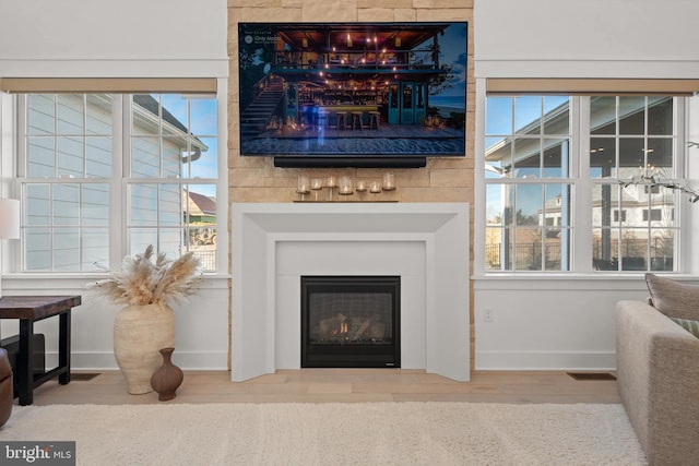 living room with visible vents, wood finished floors, baseboards, and a glass covered fireplace