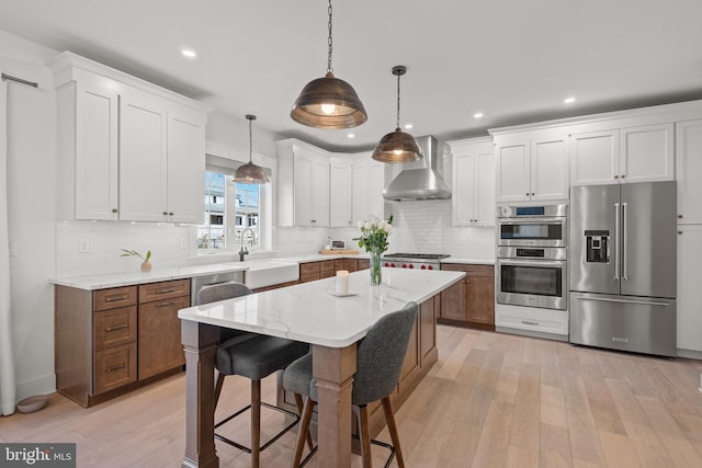 kitchen with light wood-style flooring, appliances with stainless steel finishes, wall chimney range hood, and a sink