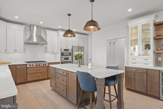 kitchen featuring appliances with stainless steel finishes, white cabinetry, wall chimney exhaust hood, and light wood-style floors