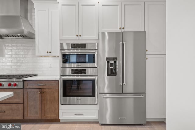 kitchen featuring decorative backsplash, appliances with stainless steel finishes, light countertops, and wall chimney range hood