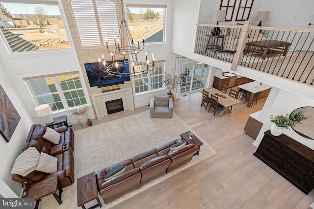 living area featuring stairway, wood finished floors, a high ceiling, a glass covered fireplace, and a chandelier