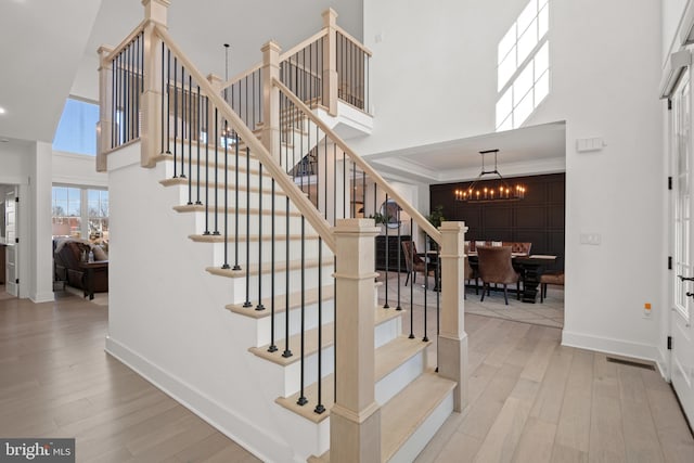 stairs with a chandelier, a high ceiling, baseboards, and wood finished floors