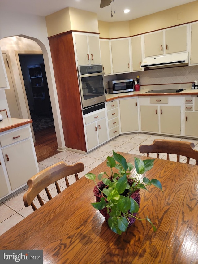 kitchen featuring tasteful backsplash, arched walkways, appliances with stainless steel finishes, extractor fan, and light tile patterned flooring