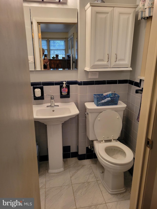 bathroom featuring toilet, marble finish floor, a sink, and wainscoting