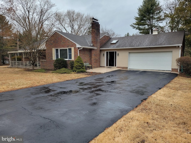 single story home featuring a garage, a chimney, aphalt driveway, a front lawn, and brick siding