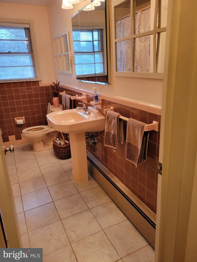 bathroom with wainscoting, toilet, a baseboard radiator, tile patterned flooring, and tile walls