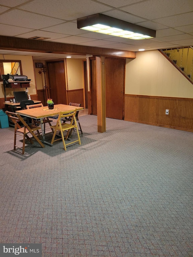 finished below grade area with a paneled ceiling, wood walls, carpet, and wainscoting