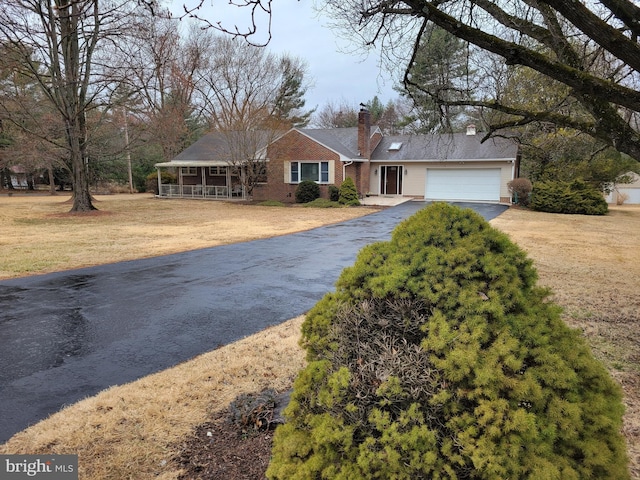 single story home with a porch, brick siding, dirt driveway, a front lawn, and a chimney