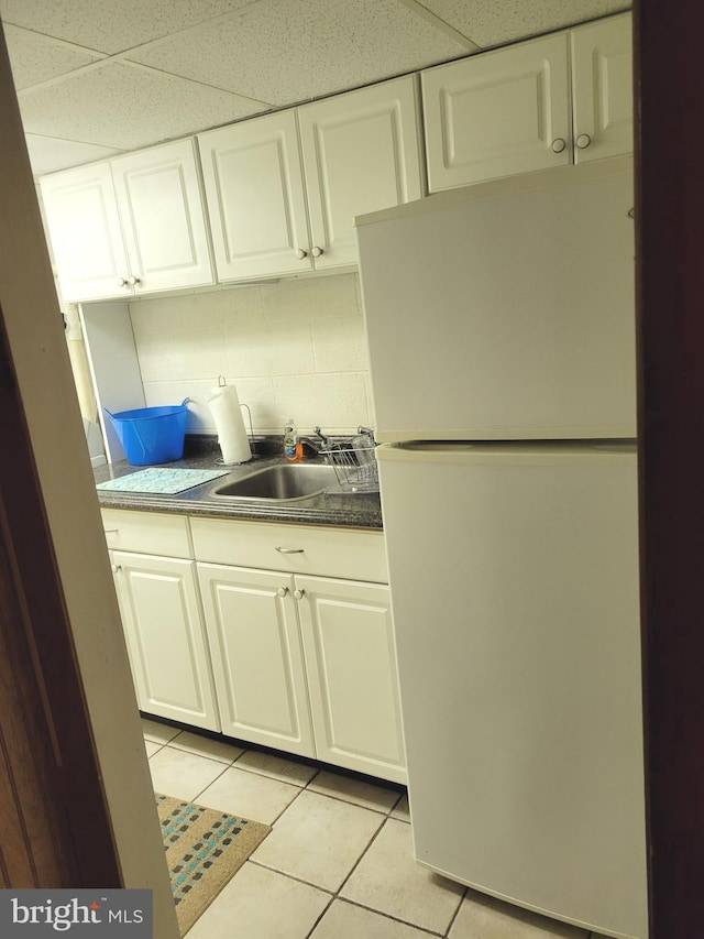 kitchen with light tile patterned floors, decorative backsplash, freestanding refrigerator, white cabinetry, and a sink