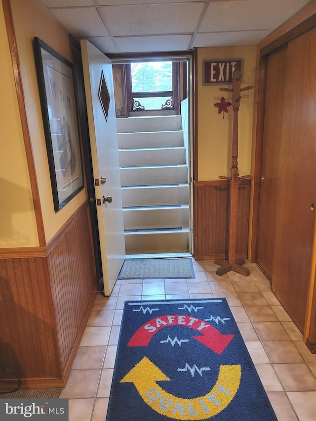 entryway with light tile patterned floors, wainscoting, a paneled ceiling, and wooden walls