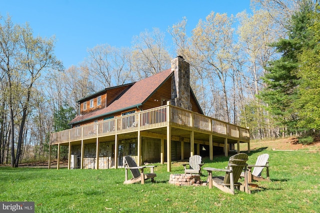 rear view of property featuring an outdoor fire pit, a lawn, a chimney, and a wooden deck