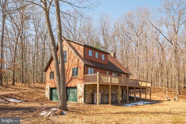 back of property with a deck, a garage, a shingled roof, stone siding, and a chimney