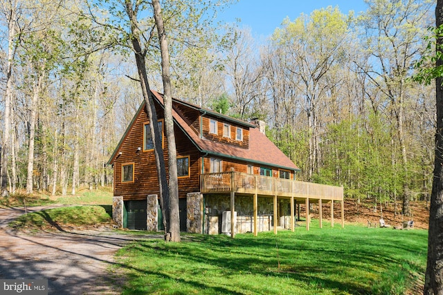 exterior space featuring a garage, stone siding, a yard, and a view of trees