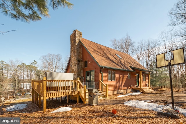 back of property with a deck, log veneer siding, roof with shingles, and a chimney