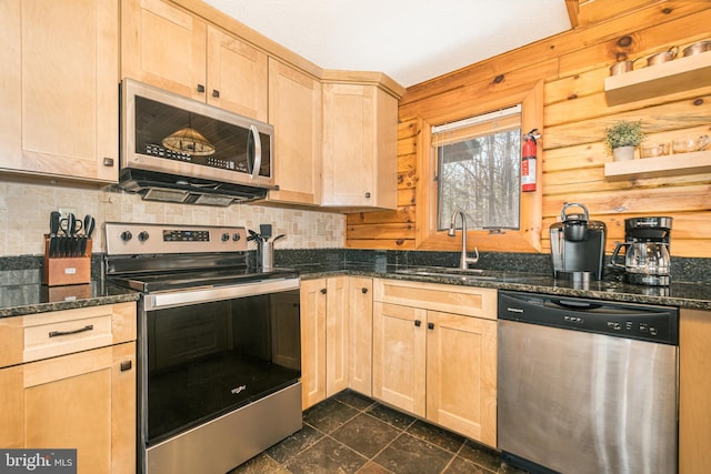 kitchen featuring light brown cabinets, wooden walls, stainless steel appliances, a sink, and decorative backsplash