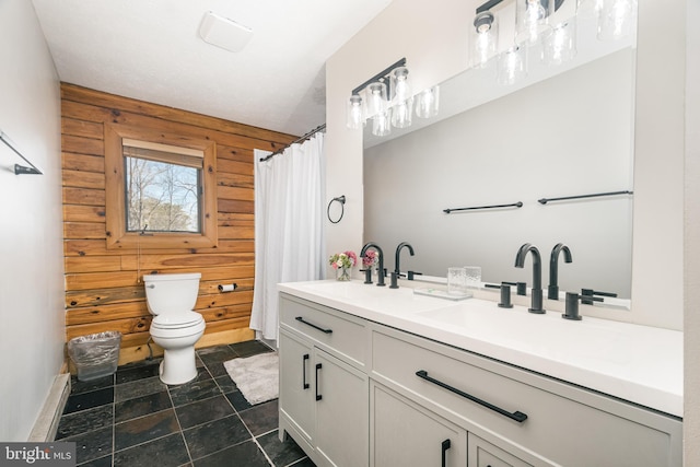 bathroom featuring toilet, double vanity, wooden walls, and a sink