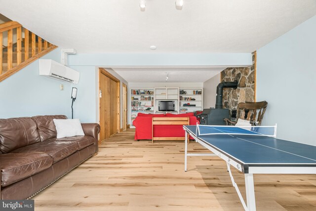 playroom featuring beam ceiling, a wall mounted air conditioner, wood finished floors, and a wood stove