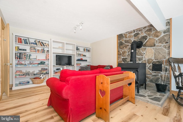 living area with beam ceiling, wood finished floors, and a wood stove