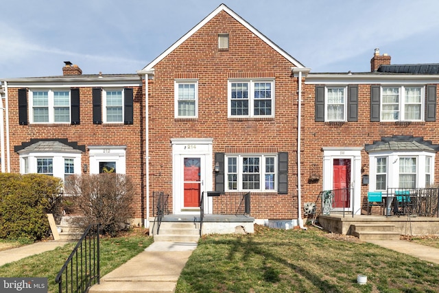 view of property featuring a front yard, brick siding, and a chimney