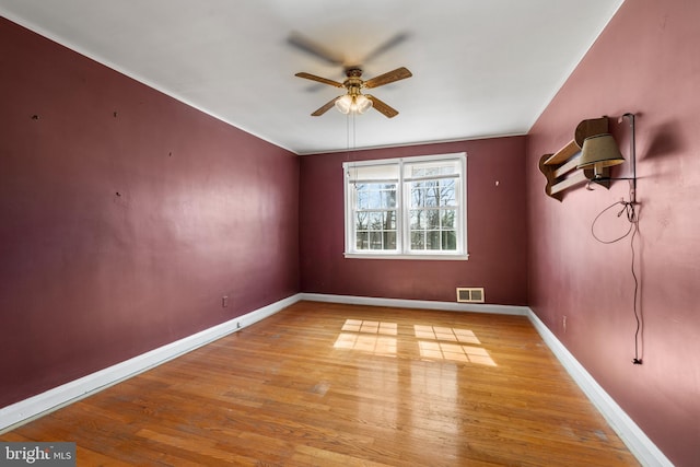 empty room featuring ceiling fan, wood finished floors, visible vents, and baseboards