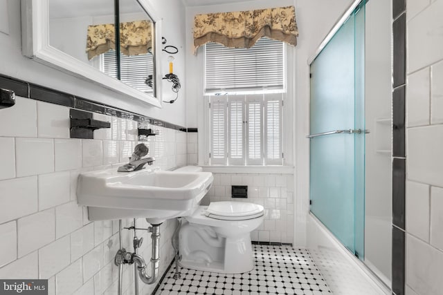 full bath with toilet, a sink, combined bath / shower with glass door, tile walls, and tile patterned flooring