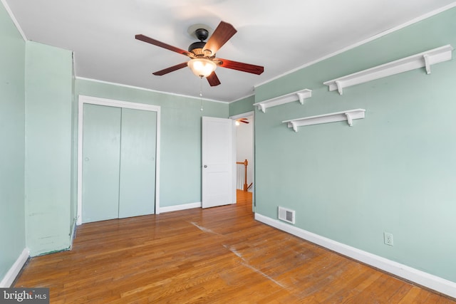 unfurnished bedroom with visible vents, baseboards, ornamental molding, wood finished floors, and a closet