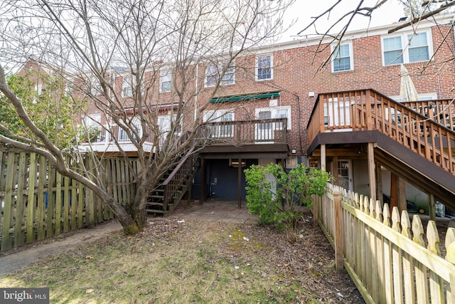 rear view of property featuring stairway, brick siding, a deck, and fence