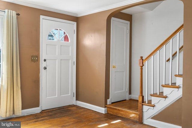 foyer featuring arched walkways, crown molding, baseboards, and wood finished floors