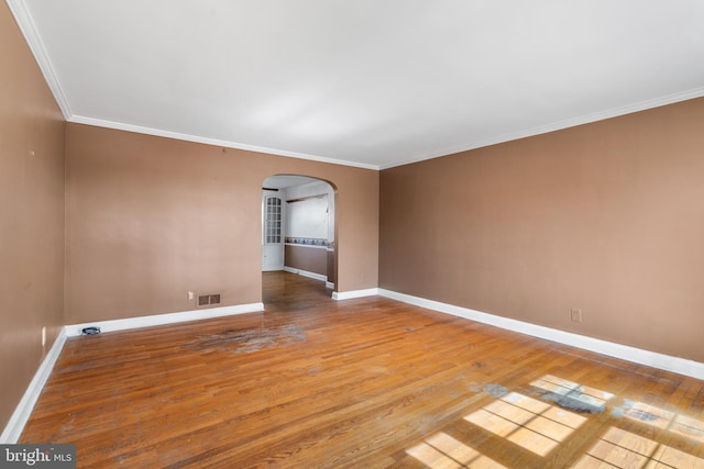 empty room featuring hardwood / wood-style floors, visible vents, baseboards, arched walkways, and crown molding