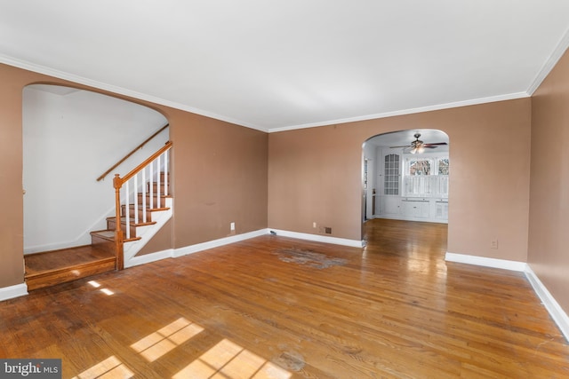 spare room with baseboards, stairs, ornamental molding, wood finished floors, and arched walkways