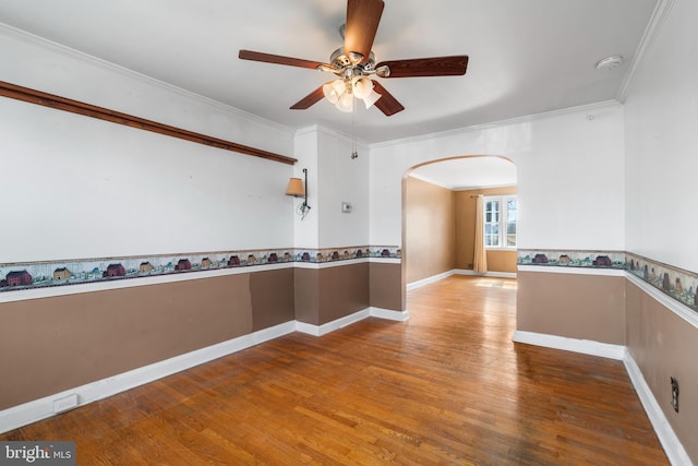 spare room featuring ornamental molding, wood finished floors, arched walkways, baseboards, and ceiling fan