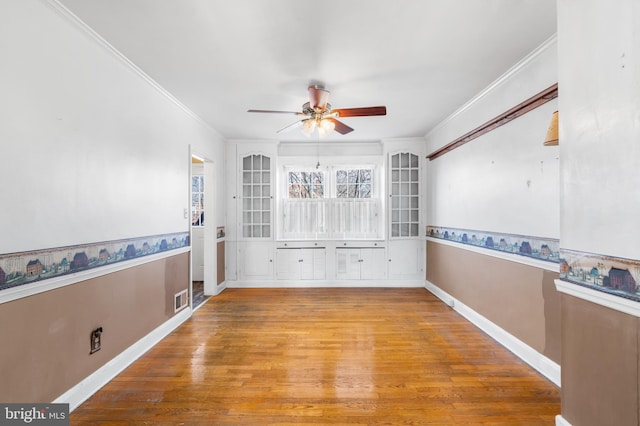 spare room with a ceiling fan, wood finished floors, visible vents, and ornamental molding