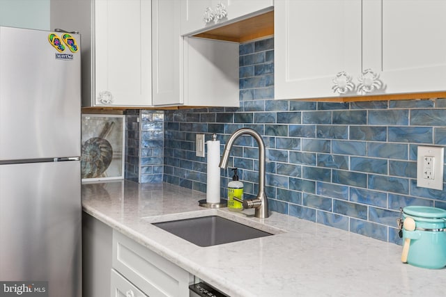 kitchen featuring tasteful backsplash, freestanding refrigerator, white cabinets, a sink, and light stone countertops