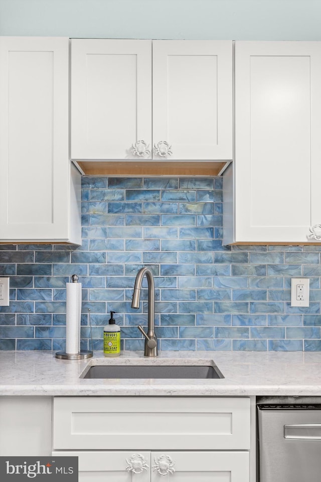 kitchen featuring tasteful backsplash, white cabinetry, a sink, and dishwasher