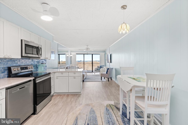 kitchen with stainless steel appliances, light countertops, white cabinetry, ceiling fan, and a peninsula