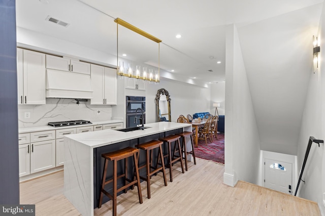 kitchen with visible vents, dobule oven black, custom range hood, a sink, and stainless steel gas cooktop