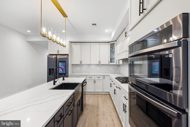 kitchen featuring white cabinetry, stainless steel fridge with ice dispenser, double wall oven, gas stovetop, and a sink