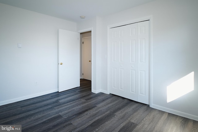 unfurnished bedroom featuring a closet, dark wood-style flooring, and baseboards