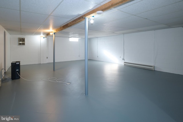 basement with concrete block wall, a baseboard heating unit, and a drop ceiling