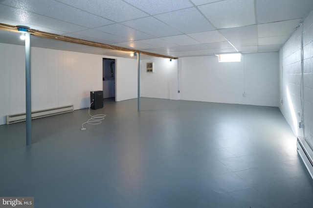 basement featuring a paneled ceiling, baseboard heating, and concrete block wall