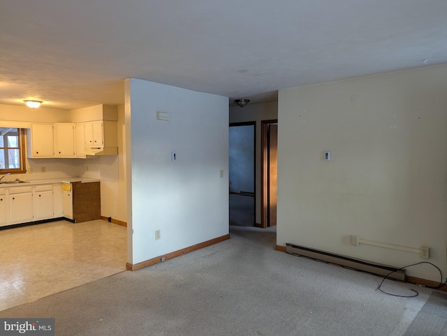 interior space with a baseboard heating unit, light carpet, a sink, and baseboards