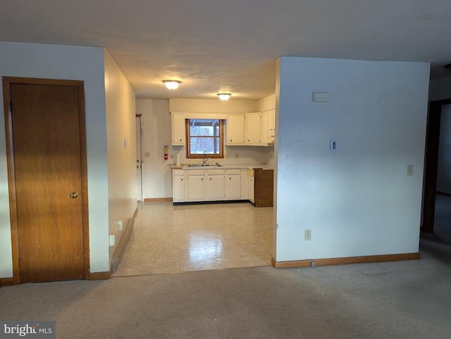 kitchen featuring light countertops, light colored carpet, white cabinetry, a sink, and baseboards