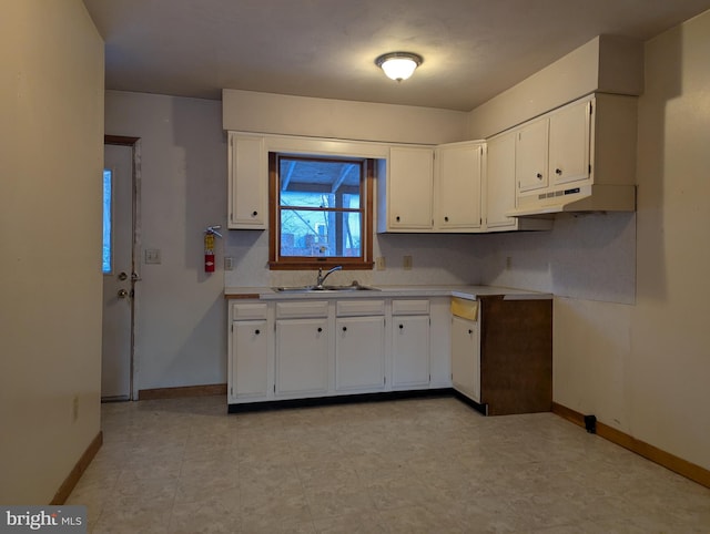 kitchen featuring under cabinet range hood, a sink, white cabinetry, baseboards, and light countertops