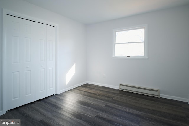 unfurnished bedroom featuring dark wood-type flooring, a baseboard radiator, a closet, and baseboards