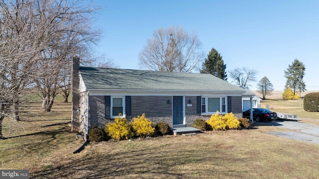 view of front of house featuring aphalt driveway, a front lawn, a chimney, and an attached garage